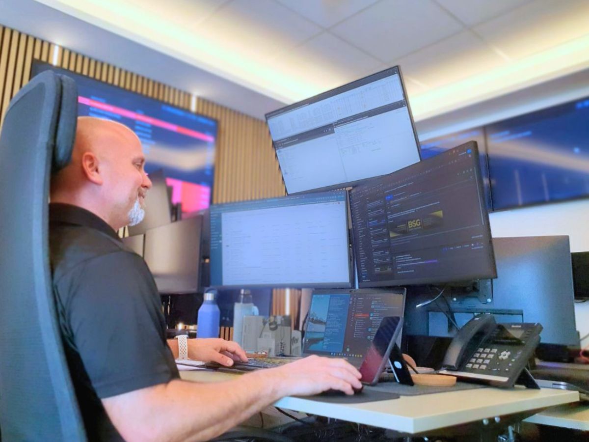 IT professional managing multiple systems from a modern multi-screen workstation in a business environment